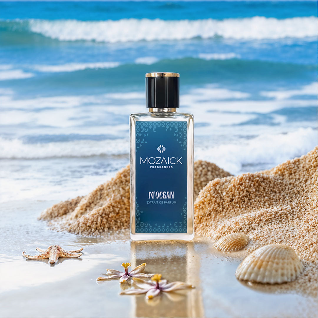 M'OCEAN Extrait de Parfum 50 ml by MOZAICK – bottle on a sandy beach with shells and the sea behind